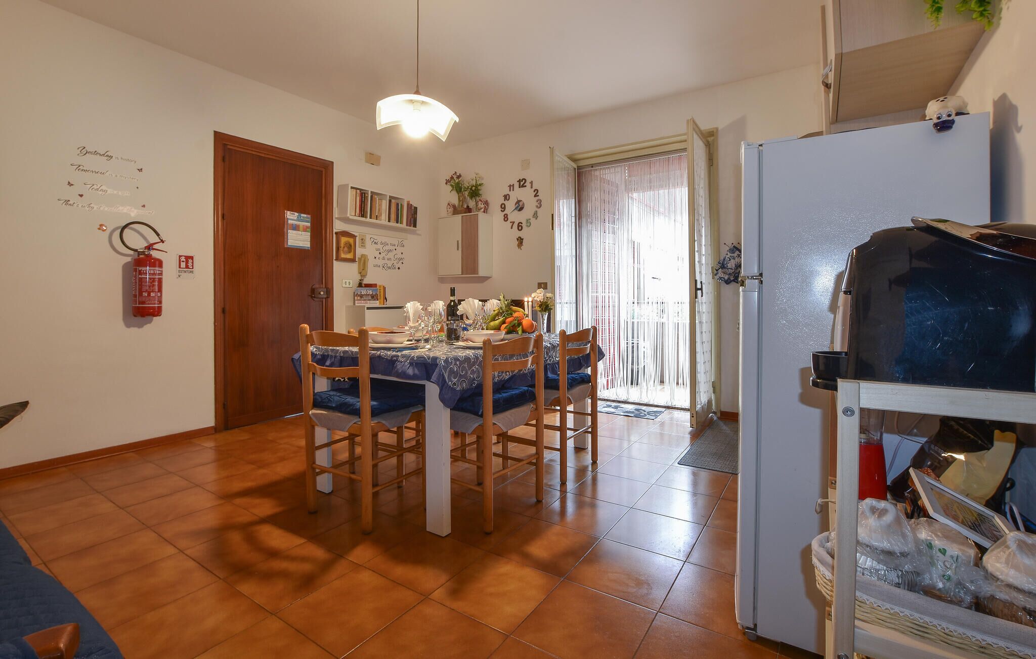 Un comedor con una mesa dispuesta para cuatro personas, un refrigerador y un extintor en la pared.