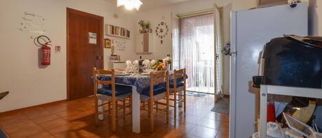 Un comedor con una mesa dispuesta para cuatro personas, un refrigerador y un extintor en la pared.