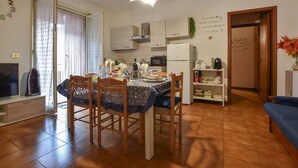 Una zona de menjador amb una taula preparada per a quatre, cuina amb electrodomèstics moderns i un ambient tranquil de sala d'estar amb un sofà.