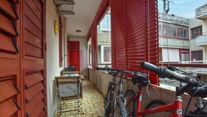 Un passadís estret amb persianes vermelles, una bicicleta i una taula petita amb una cadira.