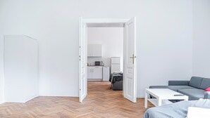 A modern, minimalist room with a wooden herringbone floor, a grey sofa, a white coffee table, and a bed with a grey blanket. - Stylish 2BR Apt Near AKH Easy Center (Vienna)