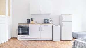 A compact kitchenette with a stove, microwave, and refrigerator, wooden flooring, and white cabinetry. - Stylish 2BR Apt Near AKH Easy Center (Vienna)