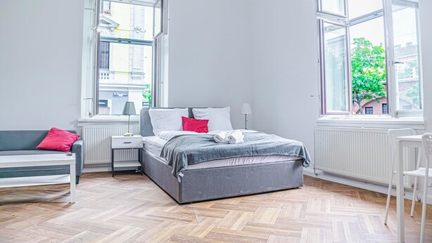 A bedroom with a bed, a bench, a chair, and large windows. - Stylish 2BR Apt Near AKH Easy Center (Vienna)
