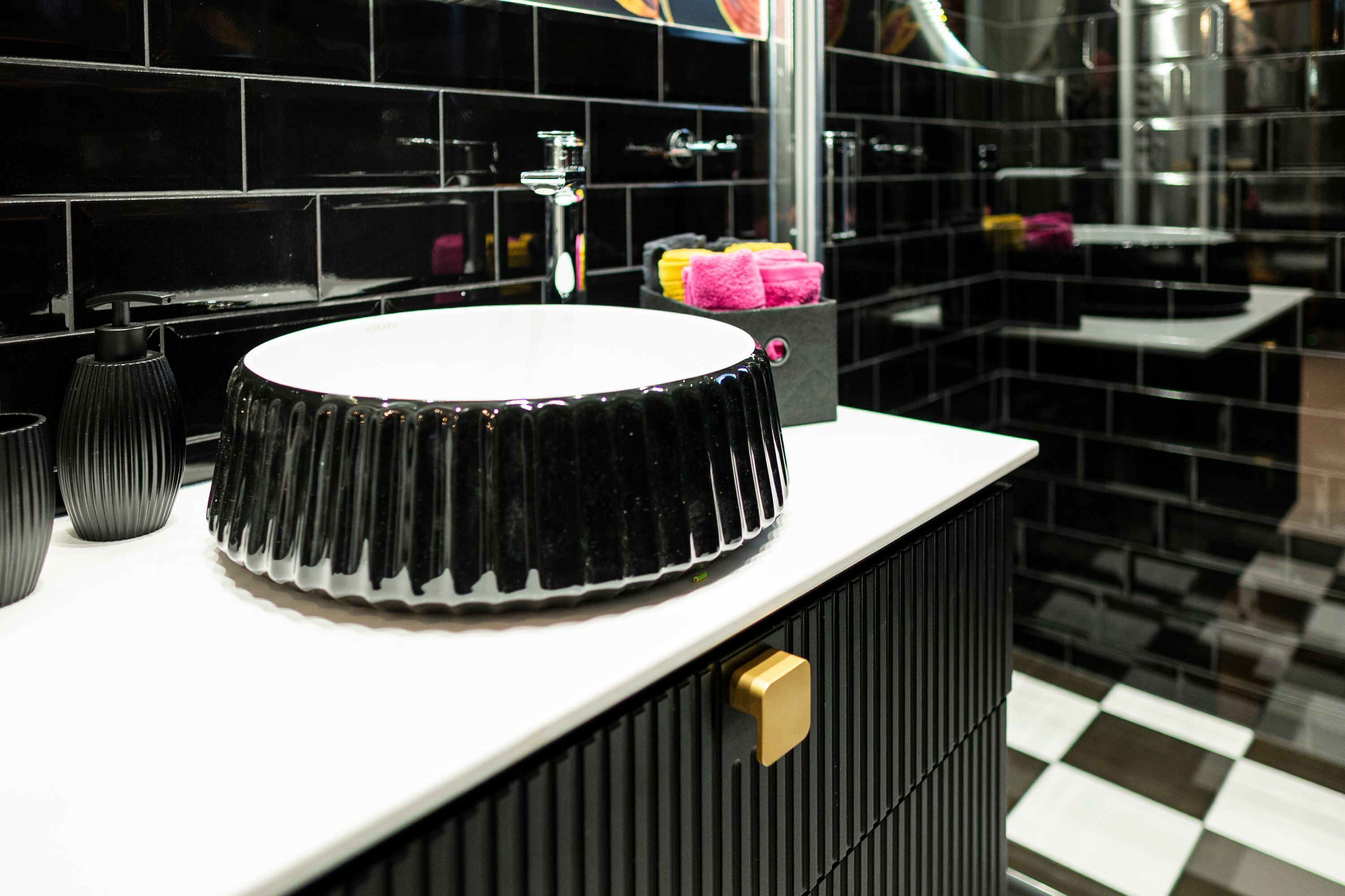 Une salle de bain moderne avec un sol à carreaux noirs et blancs, un lavabo noir à motifs en relief et une poignée de porte dorée.