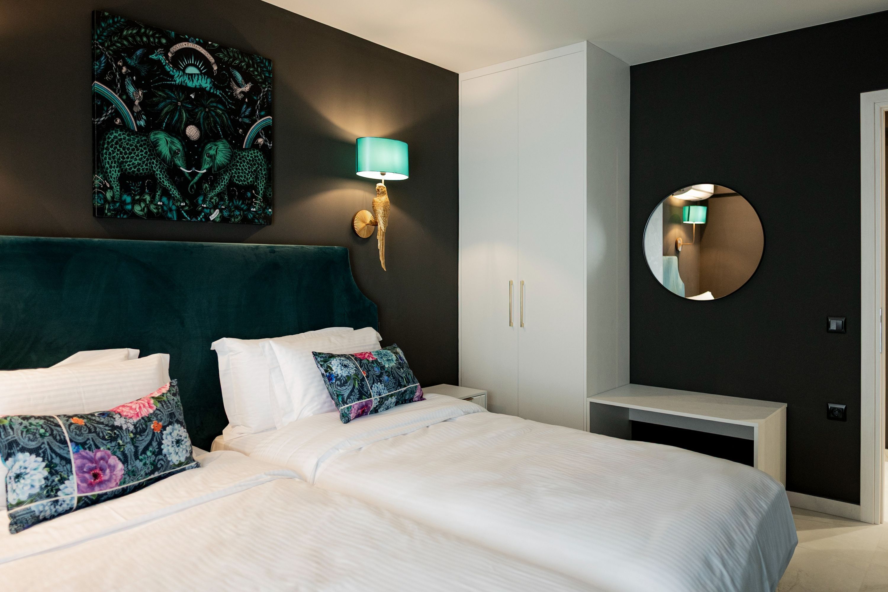 Une chambre à coucher moderne avec un grand lit, une lampe fixée au mur, un miroir rond et un tableau décoratif.