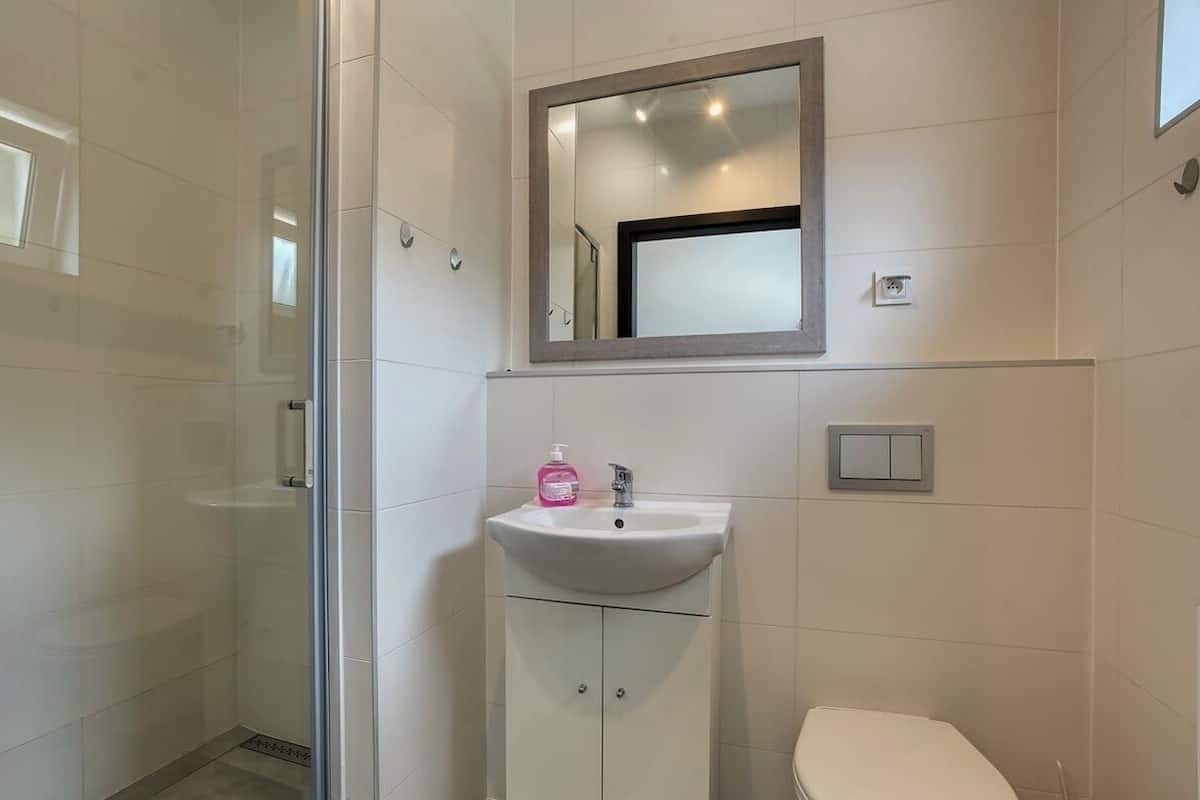 A modern bathroom with a glass shower enclosure, a white sink with a mirror above it, and a toilet.