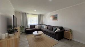 Un salon moderne avec un canapé d’angle, une table basse ronde, un téléviseur et une petite table d’appoint sur laquelle est posée une enceinte.