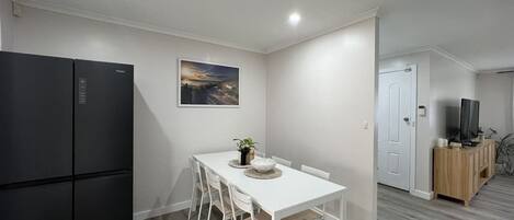 A compact kitchen with a black refrigerator, a white dining table with chairs, and a wooden cabinet with a television.