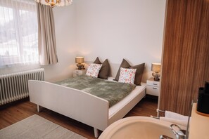 A modern bedroom with a bed, bedside lamps, a radiator, and a bathroom with a sink and mirror.