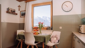 Un coin repas avec une table dressée pour deux personnes, une horloge au mur et une fenêtre donnant sur les montagnes.