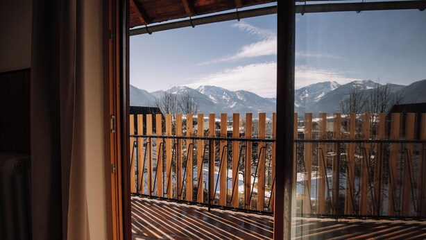 Une vue depuis un balcon avec une balustrade en bois, un paysage montagneux en arrière-plan et un ciel dégagé.