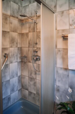 A shower with a glass door, a handheld showerhead, and a handheld shower attachment.