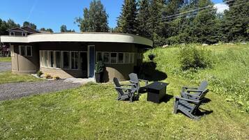 A modern building with a curved roof, a patio with Adirondack chairs, and a grassy area.