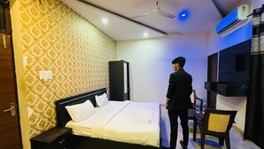 Ein Hotelzimmer mit Bett, Fernseher, Deckenventilator und einem kleinen Tisch mit Stuhl.