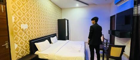 A hotel room with a bed, a TV, a ceiling fan, and a small table with a chair.