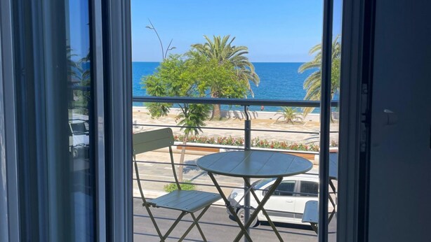 Un balcone con vista sul mare, una palma e un'auto bianca parcheggiata all'esterno.