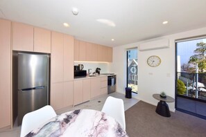 A modern kitchen with a stainless steel refrigerator, a dining area with a marble table, and a view of a street through a large window. - Freshly Styled 1BR Apartment near Te Kaha Stadium (Christchurch)