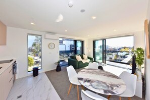 A modern living room with a green sofa, a marble coffee table, and large windows offering a city view. - Freshly Styled 1BR Apartment near Te Kaha Stadium (Christchurch)