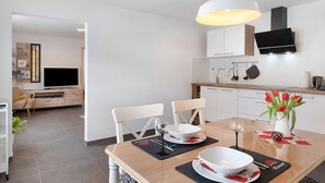 Una cocina moderna con armarios blancos, un televisor de pantalla plana y un comedor con mesa de madera, sillas y un jarrón con tulipanes rojos.