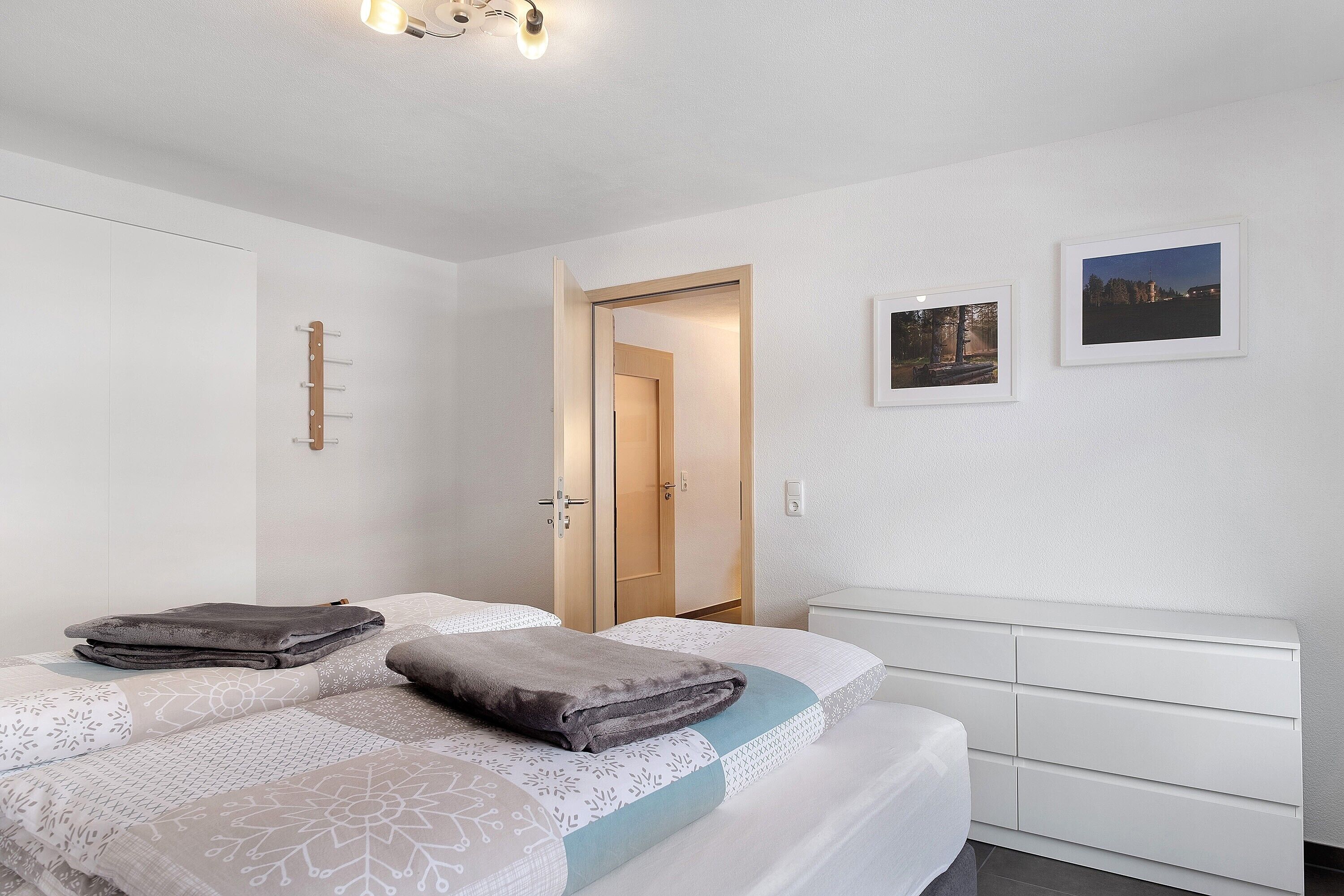 Ein Schlafzimmer mit zwei Betten, einem Kleiderschrank, einem Nachttisch und einer Tür zu einem weiteren Raum.