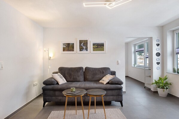 Un salon moderne avec un canapé gris, deux petites tables rondes et trois tableaux encadrés accrochés au mur.