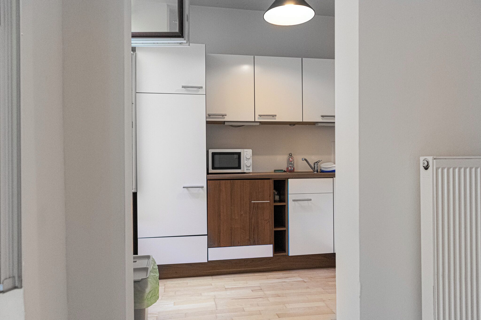 Een keuken met witte kastjes, een magnetron en een houten kast.