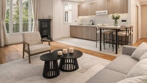 Una sala moderna con un sofá, una mesa de centro y una silla. Hay una zona de cocina con una mesa de comedor y taburetes de bar.