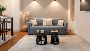 Una sala de estar moderna con un sofá gris, dos mesas negras, un jarrón con plumas de pampa y un televisor montado en la pared.