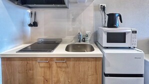 Une cuisine compacte dotée d’une hotte en acier inoxydable, d’un four à micro-ondes encastré, d’un évier et d’armoires en bois.