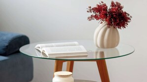 A glass-top table with a white vase and a book on it, placed on a wooden floor. - Apartment in the Center | 5 Minutes from the Old Town Square (Poznań)
