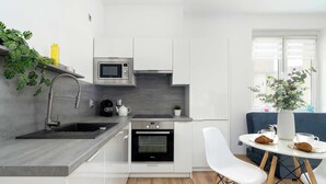 A modern kitchen with a built-in oven, microwave, and sink. There is a dining area with a table and chairs, and a window with a view. - Apartment in the Center | 5 Minutes from the Old Town Square (Poznań)