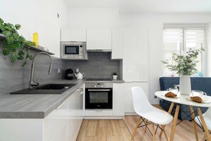 A modern kitchen with a built-in oven, microwave, and sink. There is a dining area with a table and chairs, and a window with a view. - Apartment in the Center | 5 Minutes from the Old Town Square (Poznań)