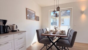 Un comedor con una mesa lista para cuatro personas, una cafetera y una ventana con persianas.
