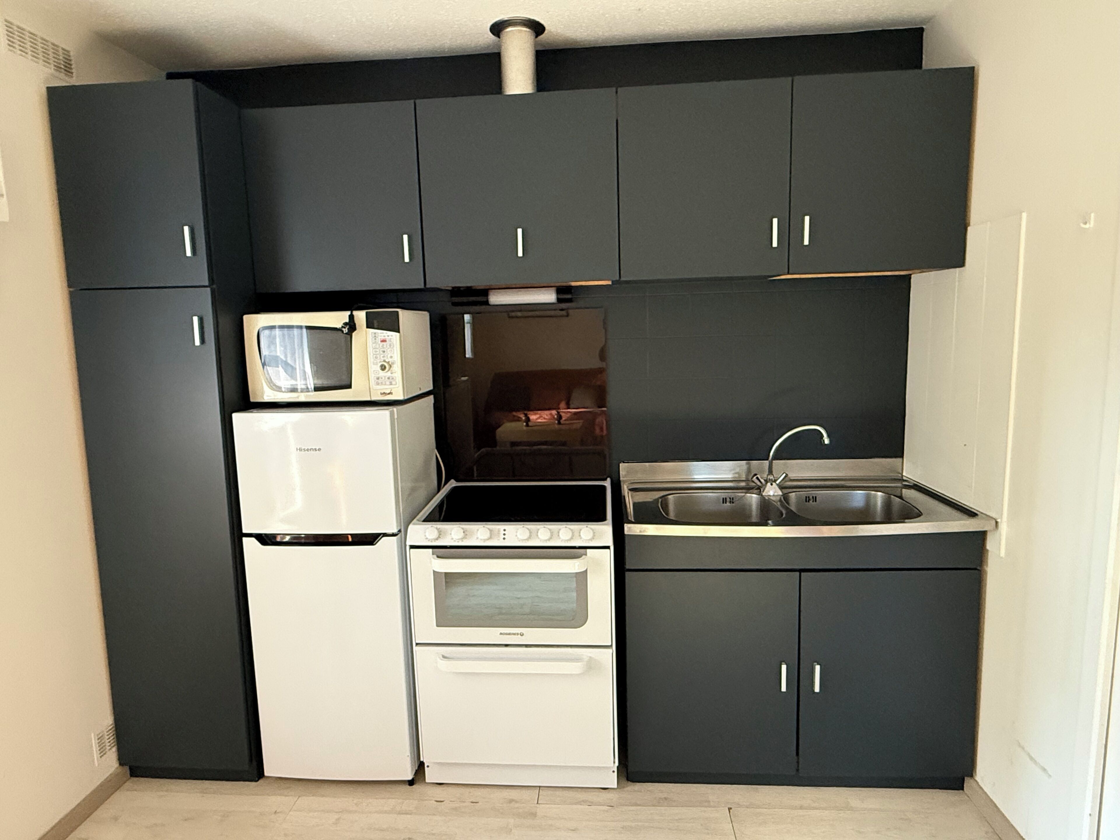 A compact kitchen with black cabinets, a microwave, a refrigerator, a stove, and a sink.