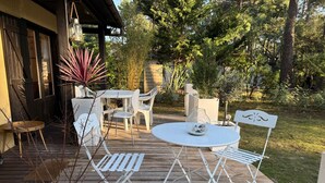 An outdoor patio with a round table and white chairs, surrounded by potted plants and a wooden deck. - South-facing Euronat studio with pool area, shops, restaurants, entertainment... (Grayan-et-l'Hôpital)