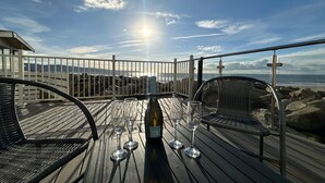 Um deck de madeira com uma mesa posta para dois, com vista para a costa rochosa.