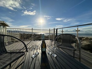 A wooden deck with a table set for two, overlooking a rocky coastline. - Sea breezes, sandy toes and dolphin Hellos (Barmouth)