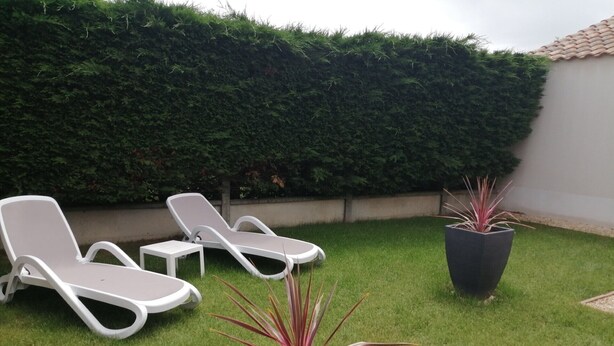 Un patio trasero con dos sillones blancos, una mesita y una planta en maceta.