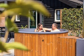 A wooden hot tub with a wooden exterior, a door, and a window. - Comfortable ground-floor accommodation for 2 persons with a private hot tub in the garden. Compact in size, yet warmly and fully furnished. (Otterlo)