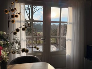 A room with a large window, a door, and a table with chairs. - Comfortable ground-floor accommodation for 2 persons with a private hot tub in the garden. Compact in size, yet warmly and fully furnished. (Otterlo)