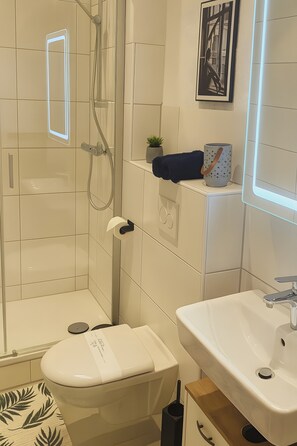 Et moderne badeværelse med bruseniche i glas, et hvidt håndvask og toilet.