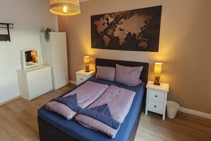 Ein Schlafzimmer mit einem großen Bett, zwei Nachttischen, einer Kommode, einer Weltkarte an der Wand und einer Hängelampe.