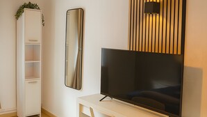 Een moderne kamer met een wit bureau, een flatscreen-televisie, een witte stoel, een hoge witte kast en een spiegel aan de muur.