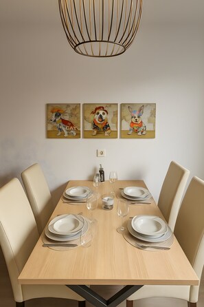 Et spisebord dækket med tallerkener, glas og bestik, omgivet af stole, med en pendel over sig og kunst på væggen.