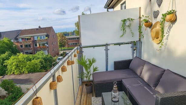 Een balkon met rieten meubilair, hangplanten en uitzicht op gebouwen.