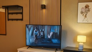 Een moderne woonkamer met een flatscreen televisie, houten vloer, een witte tv-meubel en een lamp op een bijzettafeltje.