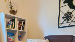 Een woonkamer met een donkerbruine bank, een witte boekenkast, decoratieve kompaswanddecoratie, en een brandende kaars in een rustieke houder.