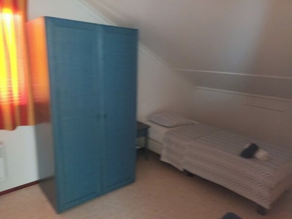 Une petite chambre avec une armoire bleue, un lit simple et une fenêtre avec des rideaux.