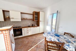 A kitchen with white cabinets, a gas stove, and a dining area with a table and chairs. - Appartamento Mare Blu - Terracina (Terracina)