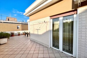 A residential patio with tiled flooring, potted plants, a sliding glass door, and a tiled wall. - Appartamento Mare Blu - Terracina (Terracina)